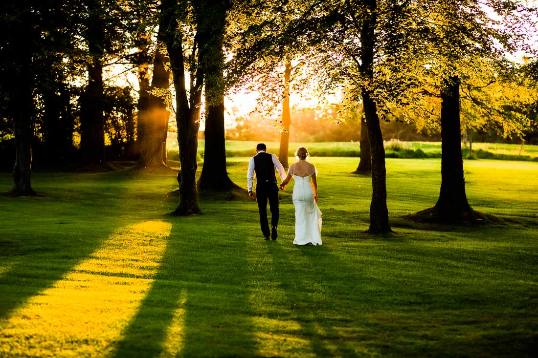 The bride and groom walk into the sunset holding hands