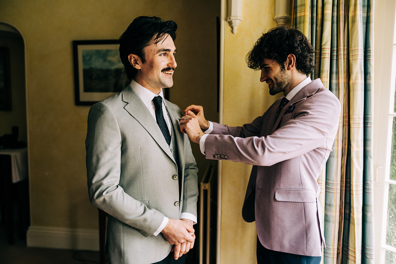 Magdalena & Ronan | Martinstown House groom having his boutonniere pinned by his best man in one of the rooms at Martinstown House