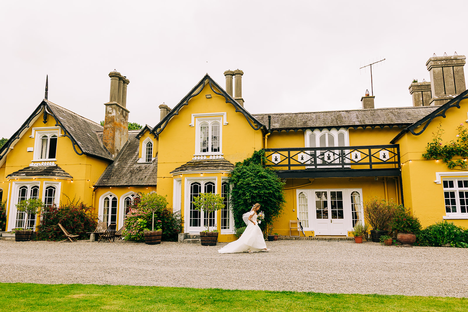Magdalena & Ronan | Martinstown House bride in wedding dress walking alone along the gravel path in front of the yellow Martinstown House facade dress flowing
