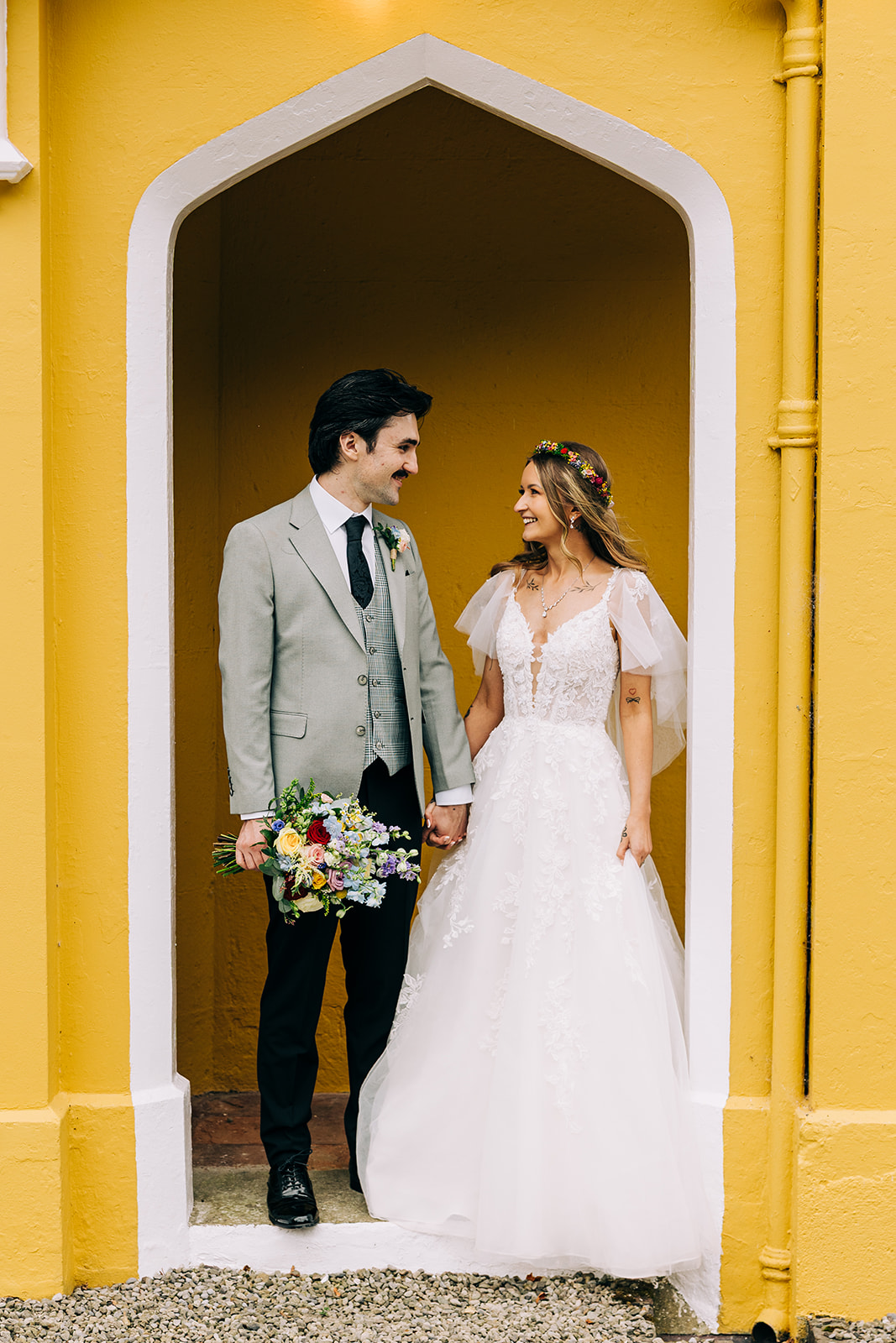 Magdalena & Ronan | Martinstown House bride and groom standing in the arched doorway of the yellow Gothic cottage at Martinstown House